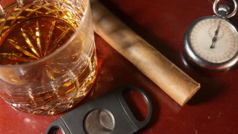 vaso de whisky, cigarro, cortador de cigarros y reloj de bolsillo antiguo sentados en la parte superior de la barra de caoba