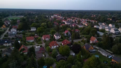 sunset residential area in brandenburg, germany, showcasing rooftops, lush greenery, and a network of roads. amazing aerial view flight panorama orbit drone