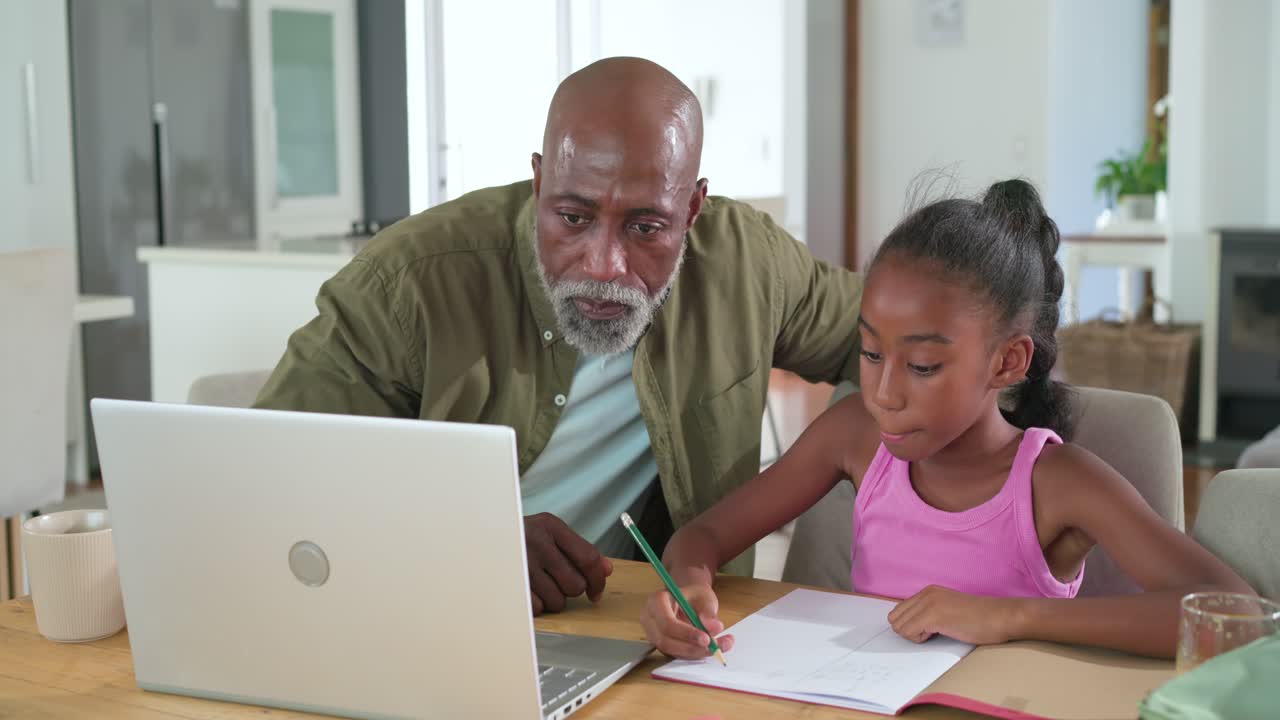 African American father guiding youth girl with homework, pointing at laptop, counting at home desk
