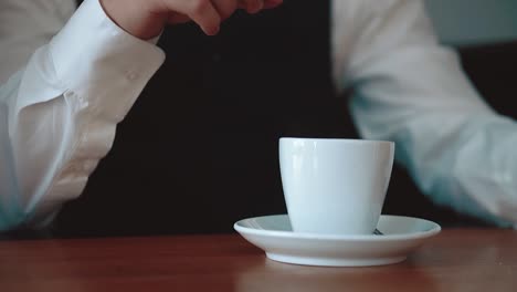 young businessman pours sugar into a mug with coffee close-up