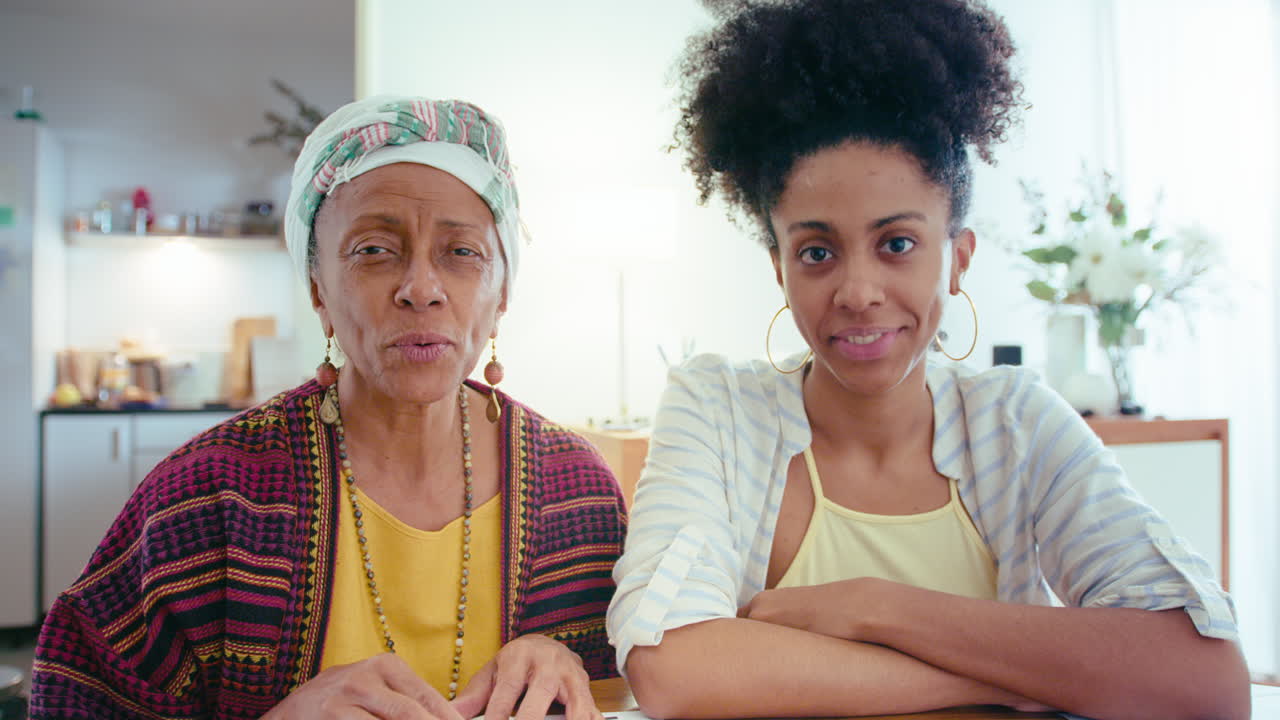 흑인 여성과 고령 어머니가 집에 앉아서 비디오 통화를 하고 있습니다.