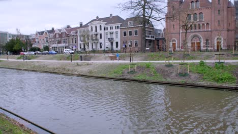 a solo runner with blue top jogs along a path by the canal in utrecht, netherlands, lined by trees and old brick buildings