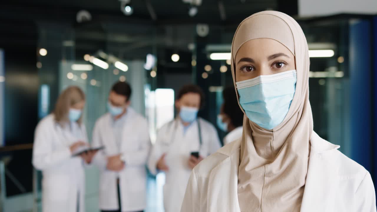 Close-up view of arabic female doctor in medical mask and hijab looking at camera standing in hospital