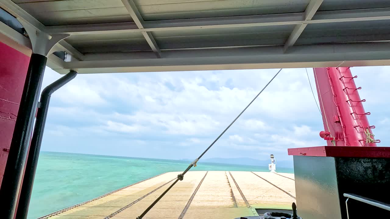 A ferry approaches a pier in Koh Samui, Thailand. Bright daylight illuminates the turquoise sea and wooden dock