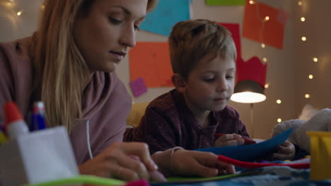 niño pequeño haciendo invitaciones para la fiesta de cumpleaños con la madre ayudando al hijo en el dormitorio colorido disfrutando de la imaginación creativa