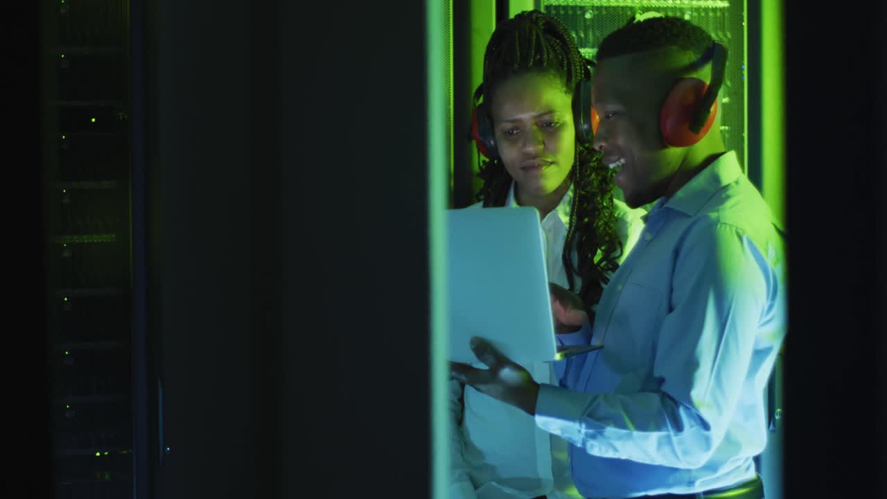 técnicos de computadoras afroamericanos usando computadoras portátiles trabajando en la sala de servidores de negocios
