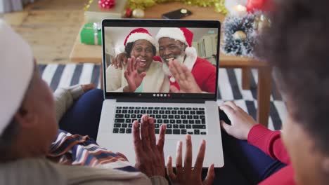 African-american-mother-and-daughter-using-laptop-for-christmas-video-call-with-couple-on-screen