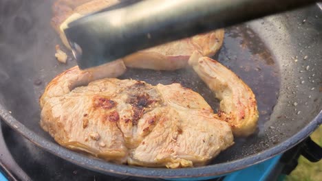 pork chops steaks cooking in hot pan outside with metal tongs moving butter for extra flavour. camping food cooked in great outdoors 4k