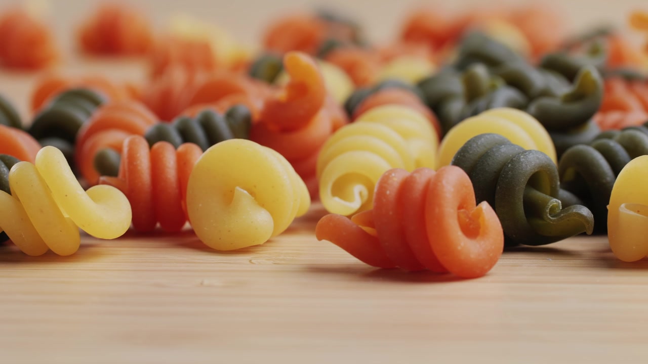 Primo piano di fusilli colorati crudi su una superficie di legno