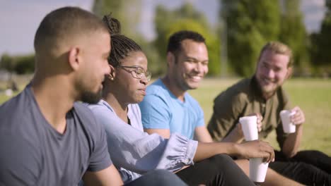 smiling colleagues sitting on lawn and drinking coffee.