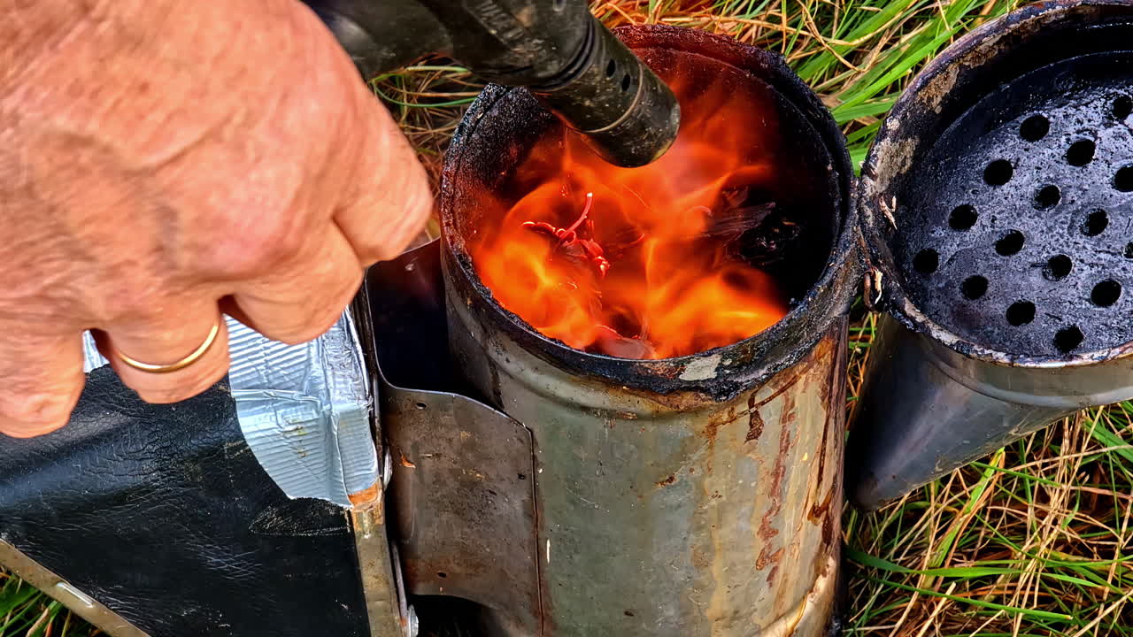 Man using torch to light charcoal in chimney for traditional outdoor cooking