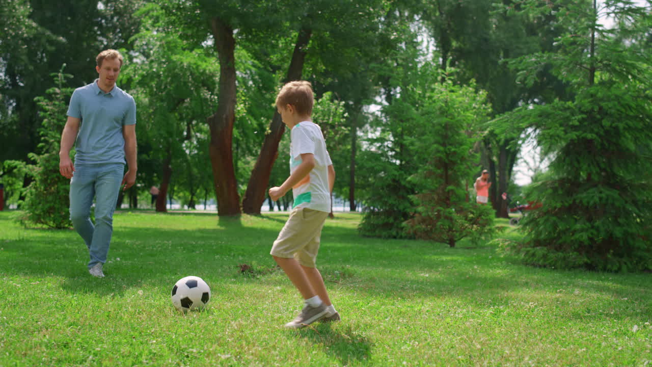 hombre deportivo pasando la pelota al hijo activo en el parque verde. el padre juega al fútbol con el niño