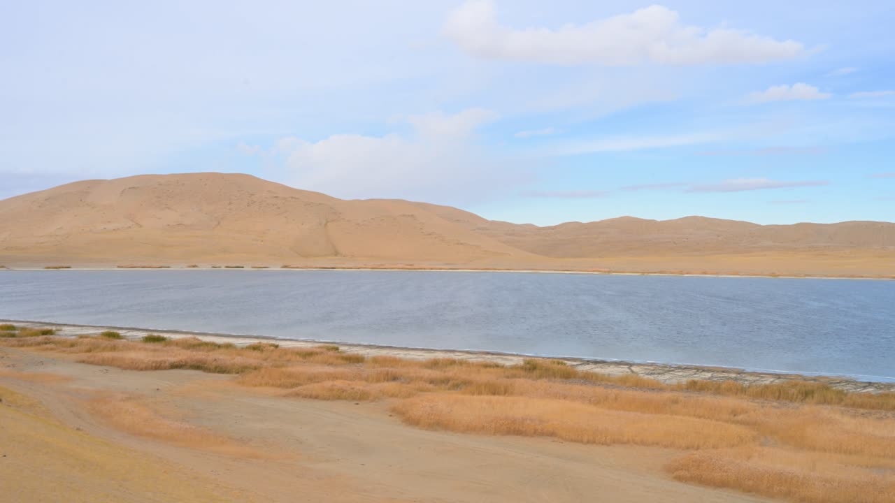 A scenic, panning left shot reveals the tranquil beauty of Durgun Nuur lake in Mongolia, capturing its golden, reed-lined shore and remote desert landscape