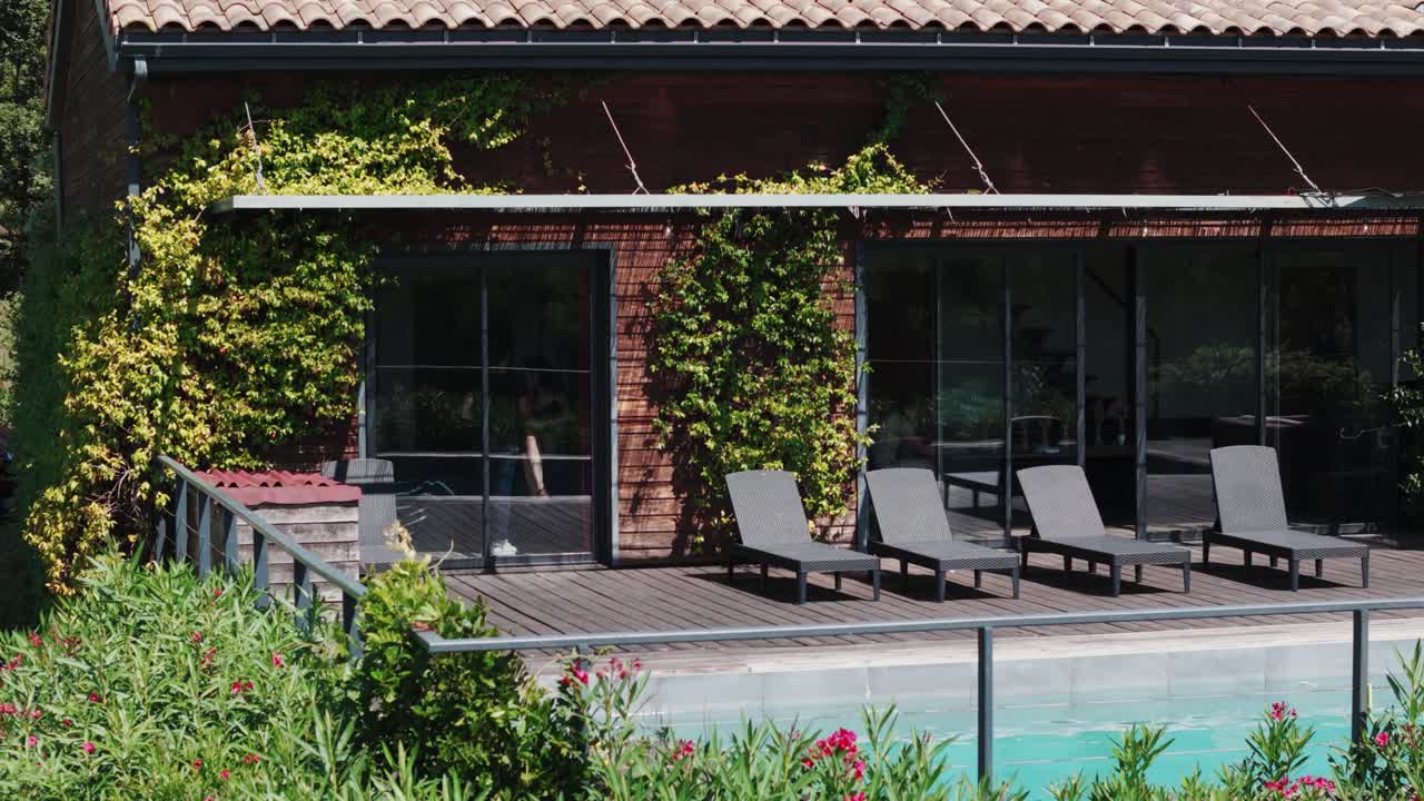 slow establishing shot of people moving within a villa with a tropical pool