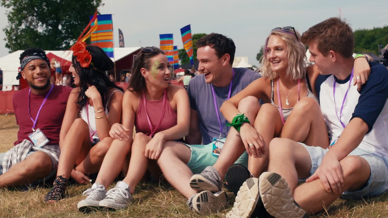Friends sitting on grass watching a gig at a music festival