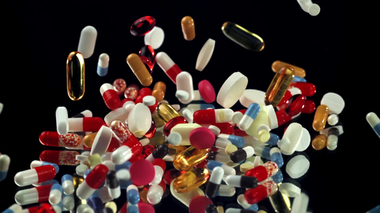 Pillole e capsule colorate che cadono e si disperdono su una superficie nera riflettente