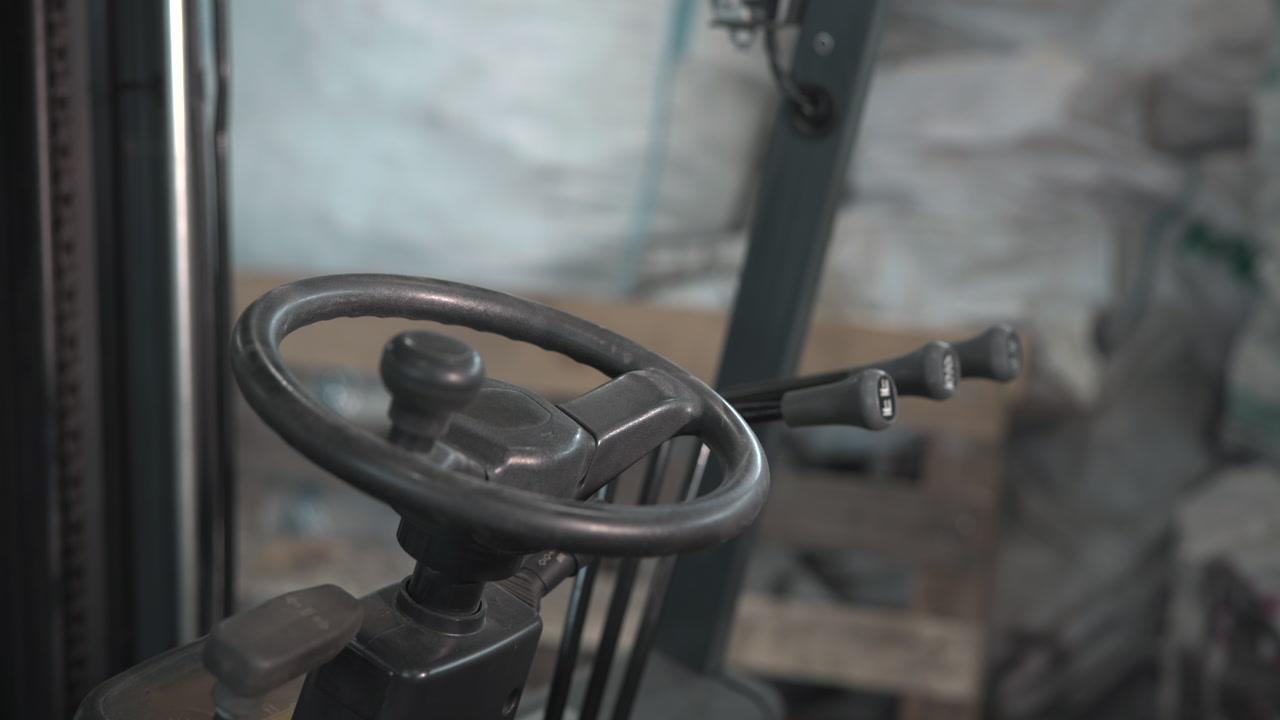 Forklift Steering Wheel And Control Levers Closeup, Worn Rubber Grips And Metal Levers, Muted Warehouse . Media