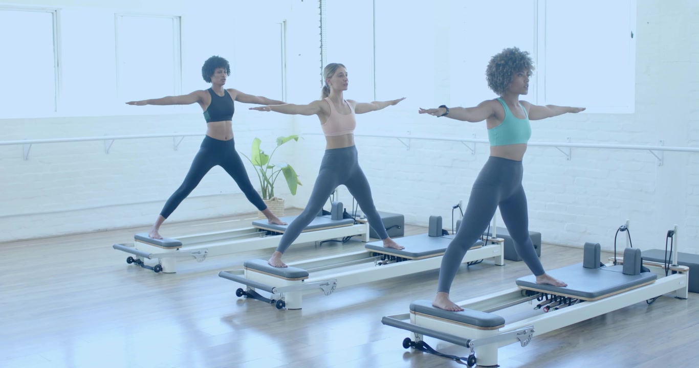 Pilates treningsgruppe utfører kriger 2-posisjon, med et rullende binært overlegg over studioet.