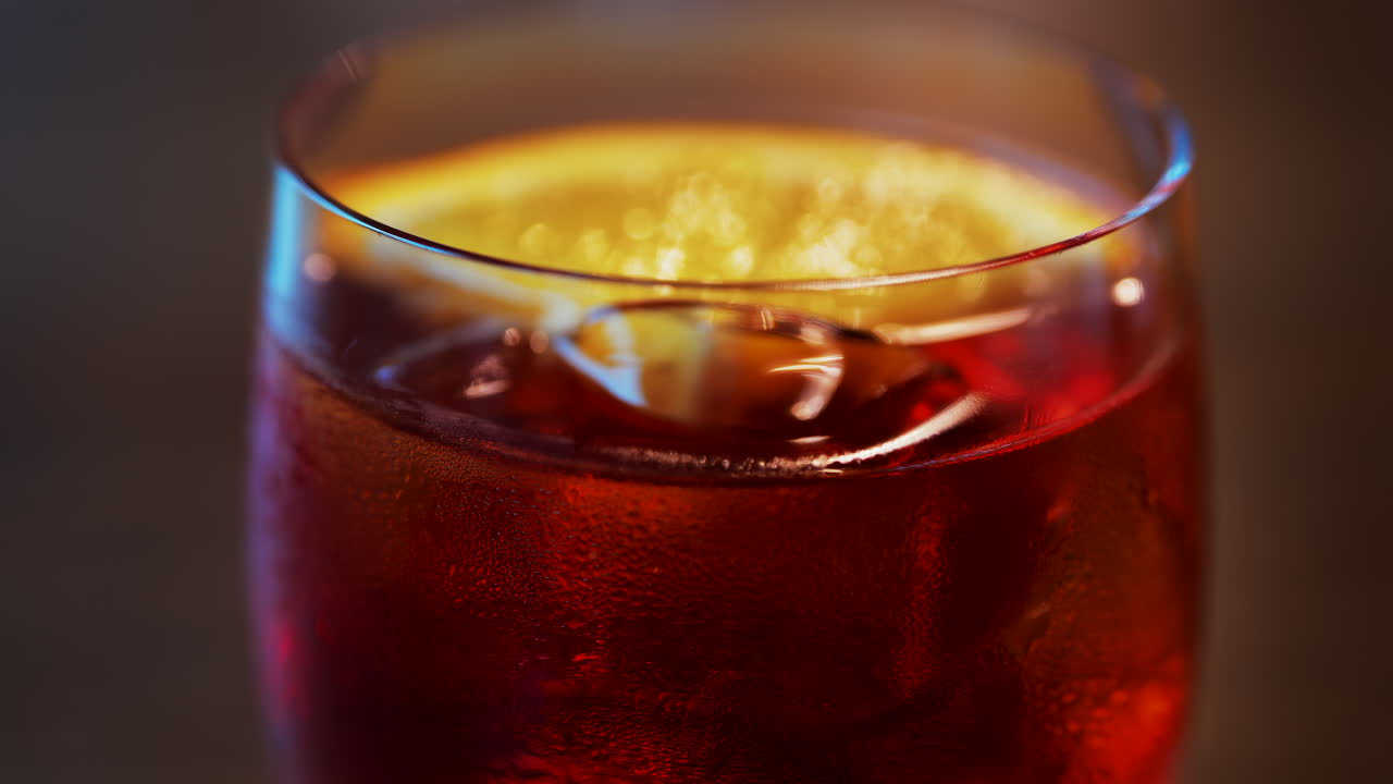 Close up of a Negroni cocktail with orange slice and ice cubes on a wooden table