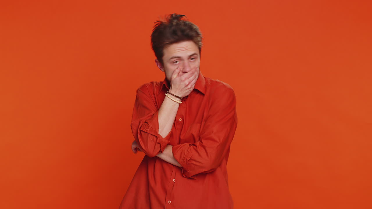 Frightened young man closing mouth with hands refusing to tell terrible secret unbelievable truth