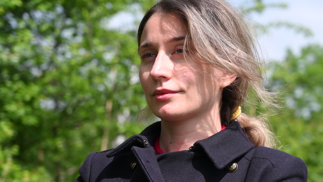 Woman with light hair standing outside, looking into the distance on a sunny day