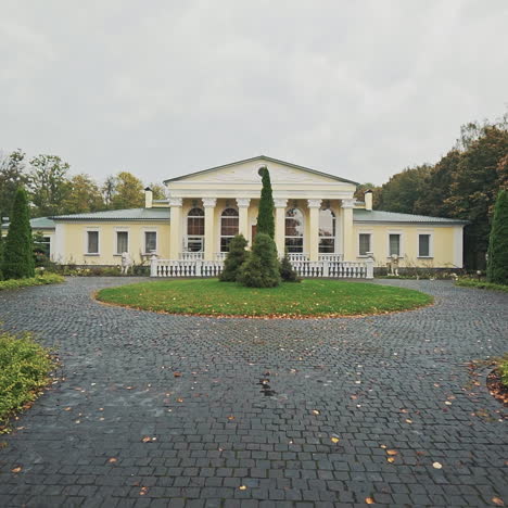 nasser bürgersteig, der zum großen leichten gebäude im park führt. schöne gasse mit grünen bäumen und einer schönen architektur im friedlichen landschaftsgarten im herbst.