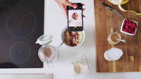 overhead shot of woman taking picture of healthy breakfast on mobile phone at home after exercise