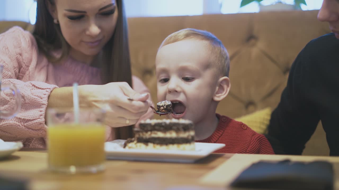 madre bonita alimenta a su hijo en su suéter rojo con cuchara de metal