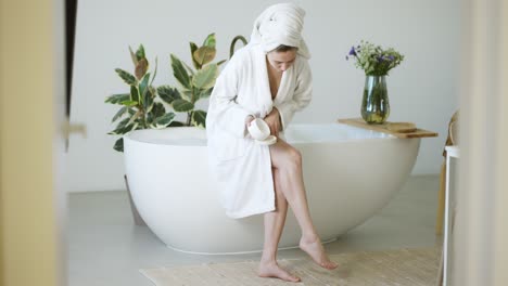 Beautiful-young-woman-applying-cream-on-her-legs-in-bathroom