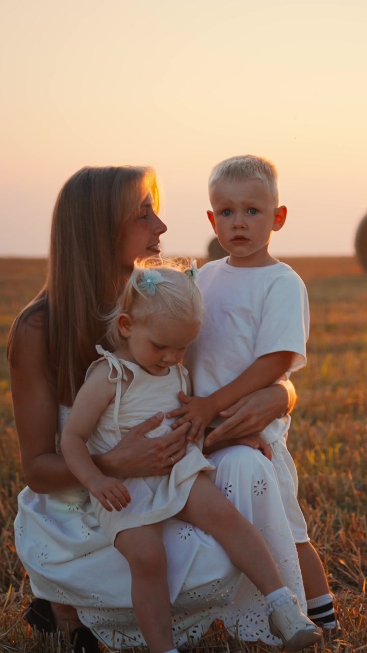 Mutter und zwei kleine Kinder sitzen bei Sonnenuntergang auf einem Feld