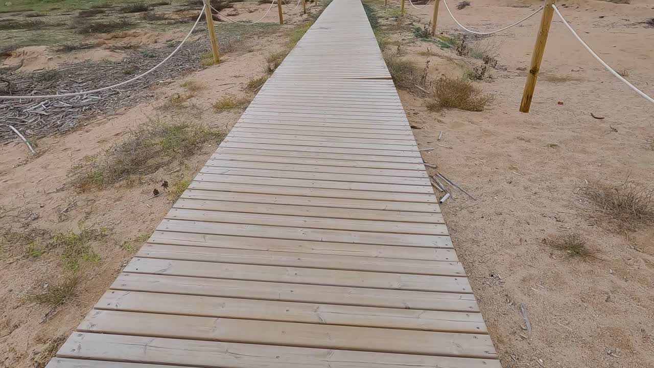 Wooden bridge over the sand direction to the beach walking in slow motion gimbal drone cloudy stormy day