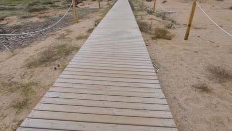 wooden bridge over the sand direction to the beach walking in slow motion gimbal drone cloudy stormy day
