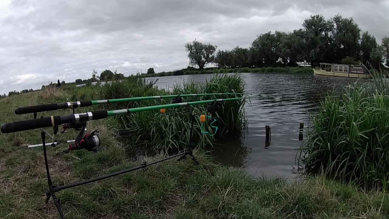 clip de cañas de pescar y un barco que pasa tomado de la orilla del río ely great ouse en inglaterra