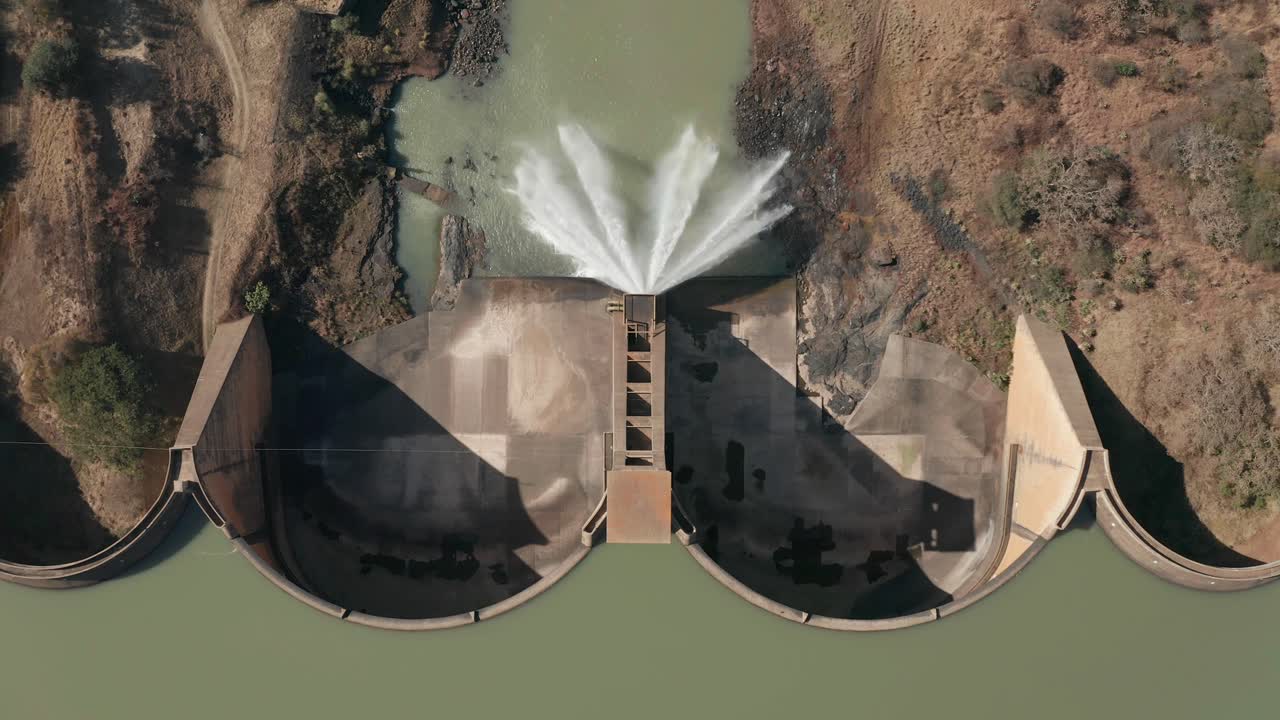 Top down aerial view arched dam wall with water spraying into river