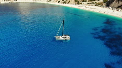 Vista-Aérea-Del-Yate-De-Lujo-En-La-Playa-De-Myrtos-Con-Bahía-Azul-En-La-Isla-De-Kefalonia,-Grecia---Disparo-De-Drones