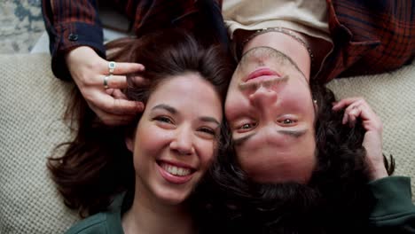 Portrait-of-a-happy-brunette-girl-and-a-guy-with-curly-hair-who-are-lying-head-to-head-on-pillows-at-home-and-smiling-in-a-modern-apartment