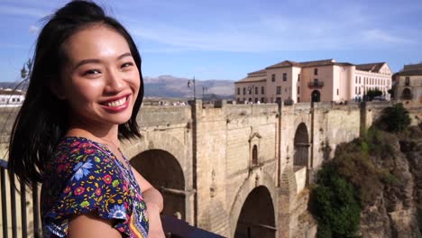 glad asian woman sitting near historic bridge in ronda