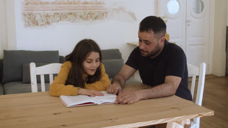 excited girl sitting at table with father and studying.