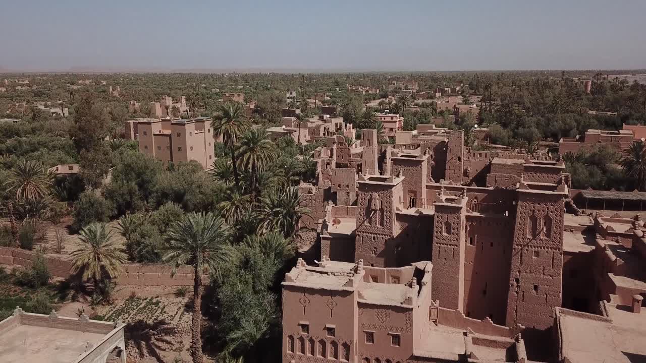 Ripresa aerea che inizia con un primo piano sui dettagli in mattoni di fango finemente lavorati della kasbah di Taourirt, per poi allargarsi e rivelare l'ampio paesaggio circostante e l'oasi di palme a Ouarzazate, in Marocco.