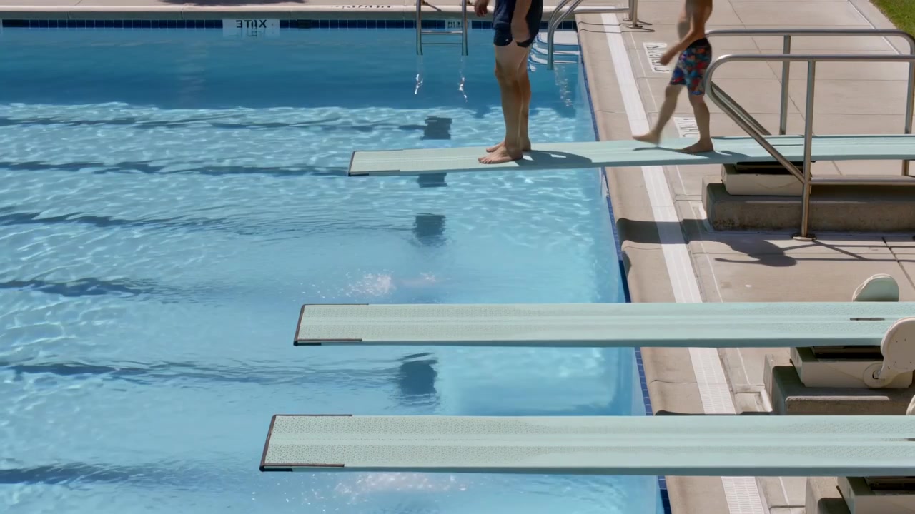Gående mand træder op på vippe ved pool, dreng følger efter for at svømme, mønstrede badebukser, kopiplads