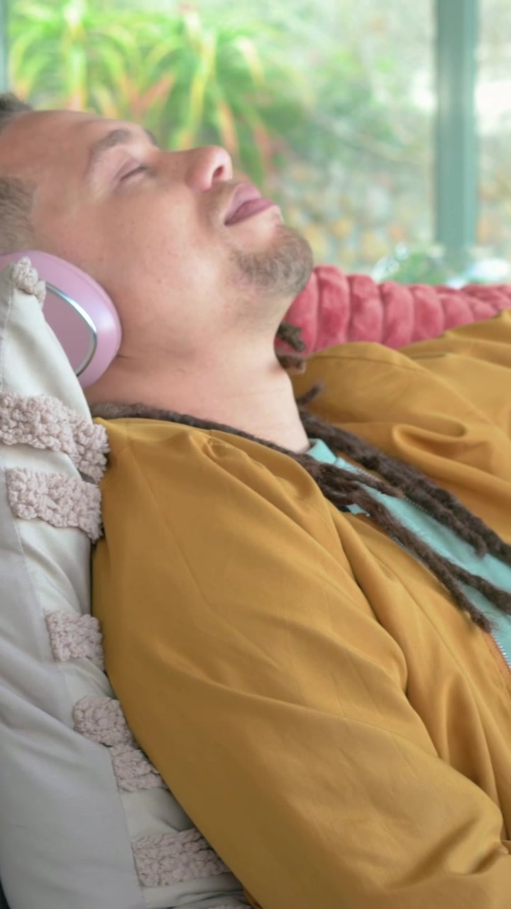Video verticale: La telecamera si allontana da un uomo con una maglietta color senape sdraiato a casa con lattine rosa, con spazio per il testo.