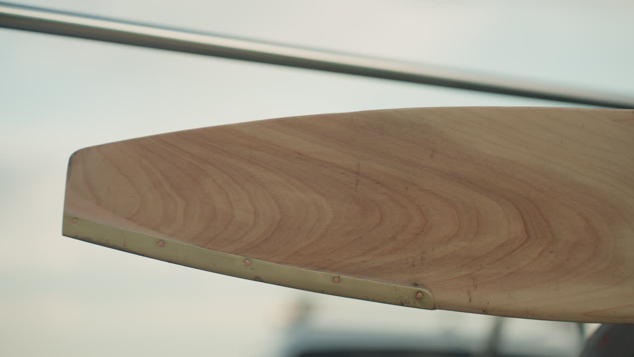 close up of wooden fan blade featuring smooth grain and brass rivet trim, shallow depth of field with blurred metal frame elements in background evoking industrial and vintage decor detail