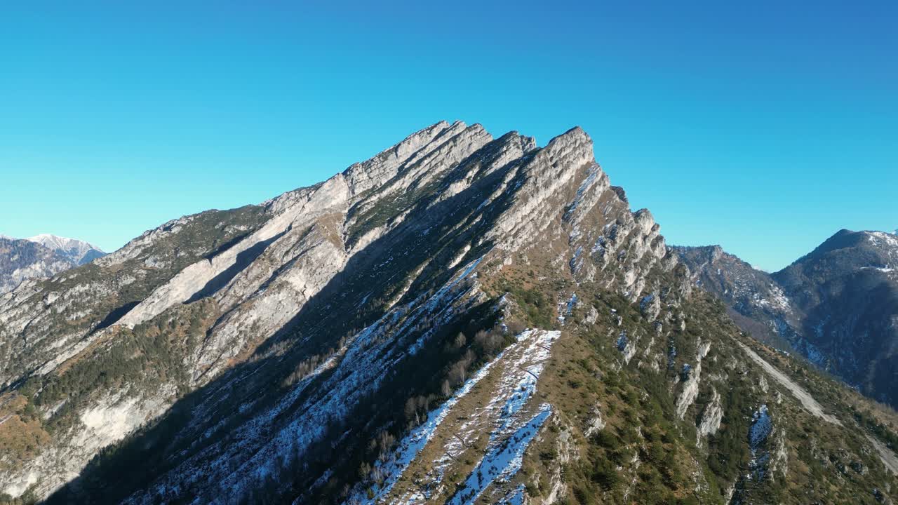 Filmato aereo realizzato con drone sopra Cluat, Italia: vette alpine spettacolari con un forte contrasto tra pendii illuminati dal sole e aree ombreggiate coperte di neve. Ideale per progetti invernali, di montagna e naturalistici cinematografici