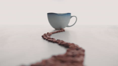 granos de café tostados colocados sobre una mesa blanca en una taza de porcelana