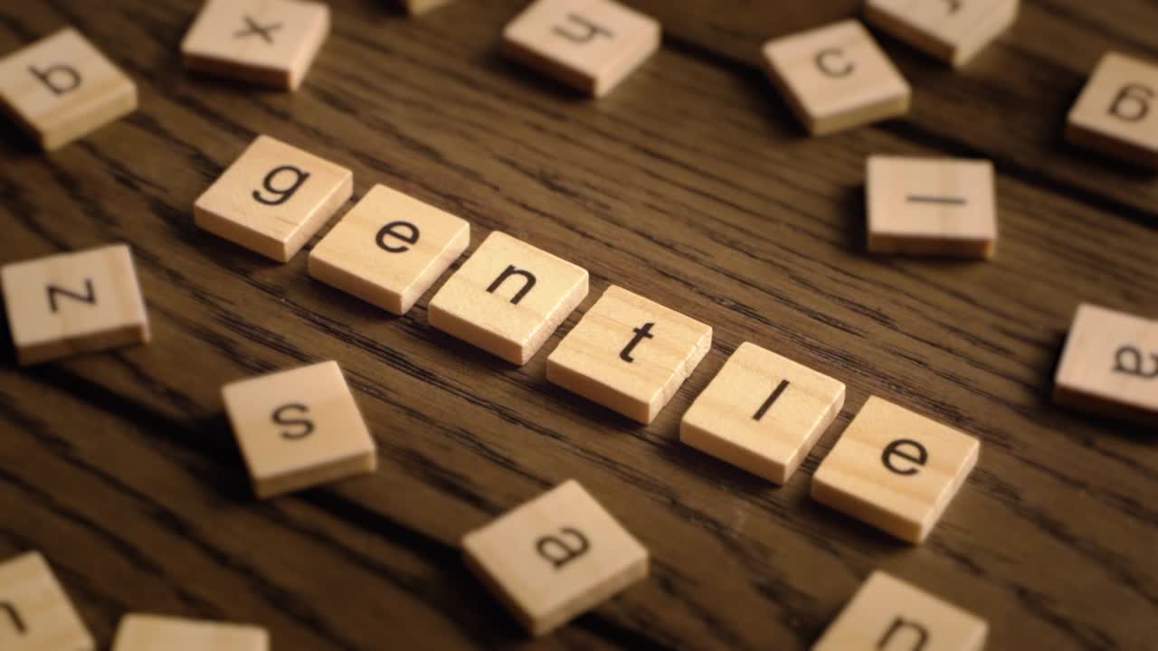 A hand carefully places wooden letter tiles to spell the word gentle on a wooden surface.