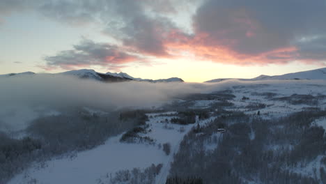 epic aerial over snowy norwegian landscape with mist, arctic circle at sunset