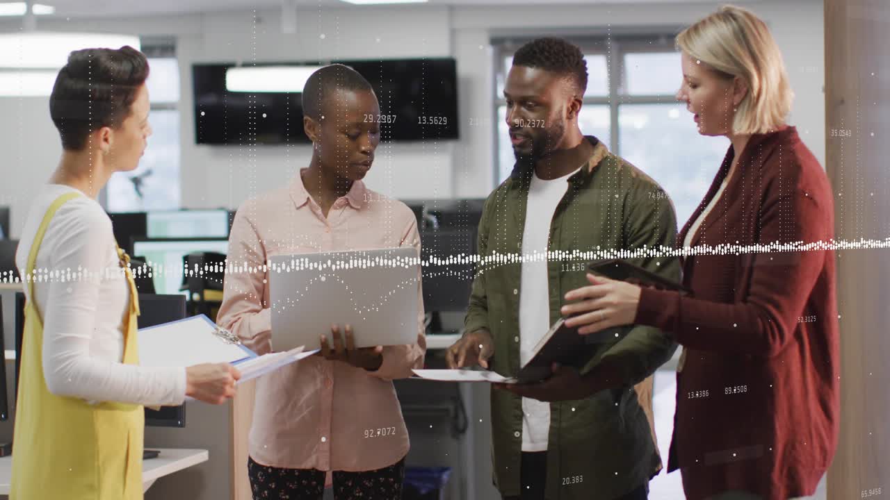 Presenter opening laptop and explaining business data as colleague marking printed charts in office