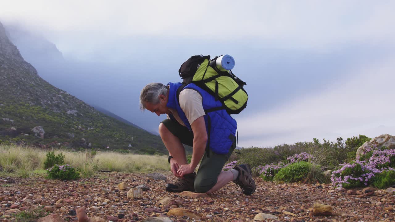 un excursionista de alto nivel con mochila atando los cordones de sus zapatos mientras hace senderismo en las montañas.