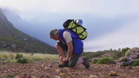 Senior-hiker-man-with-backpack-tying-his-shoe-laces-while-trekking-in-the-mountains.