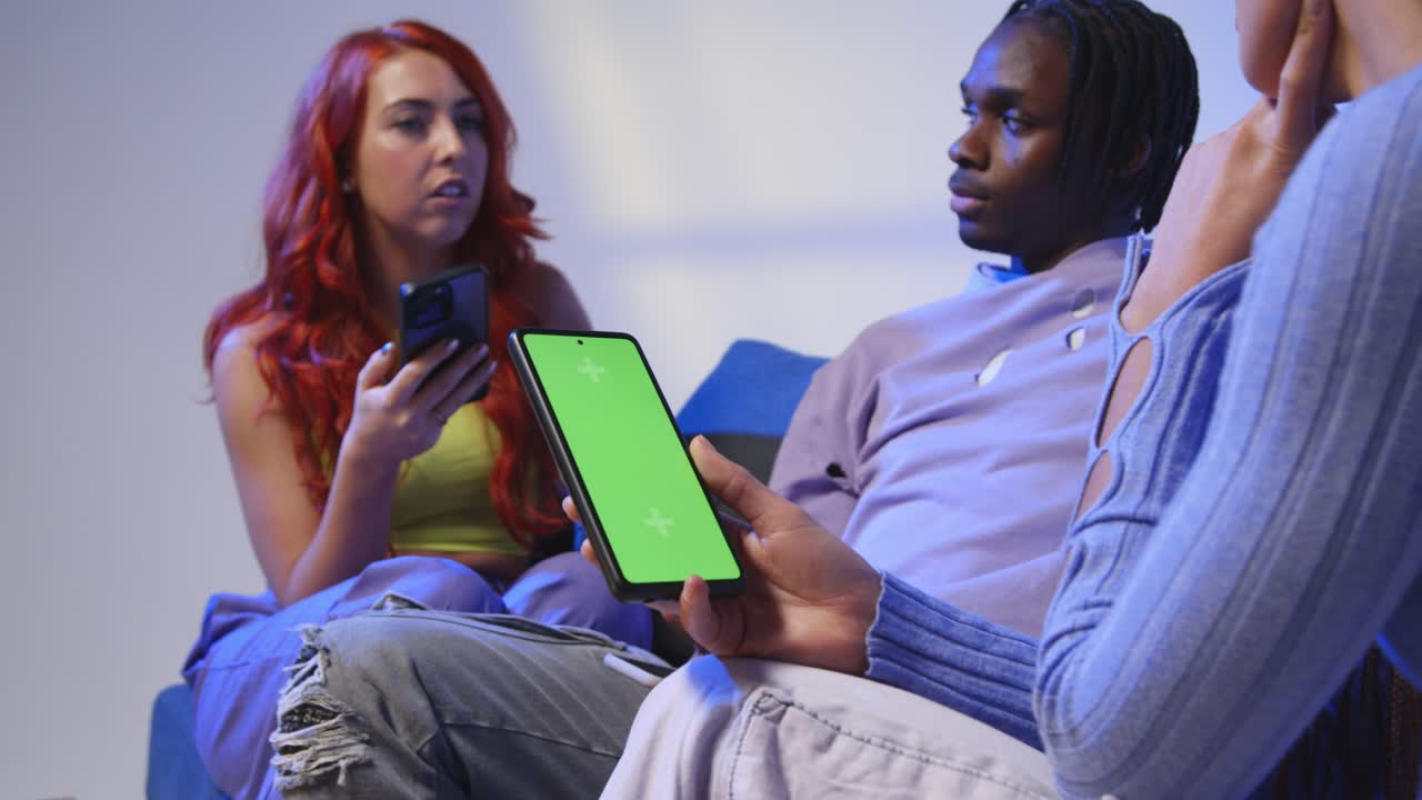 Close Up Of Woman With Green Screen Mobile Phone Sitting With Gen Z Friends Talking And Sharing Posts